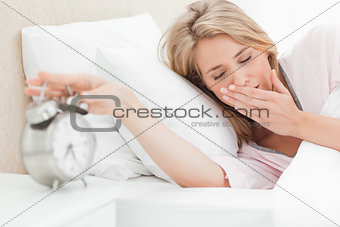 Woman with her eyes closed is reaching to silence her alarm cloc