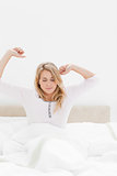 Closer shot of woman in bed sitting up with stretched out arms