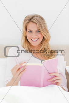 Close up shot, Woman sitting in bed, book in hand as she looks f