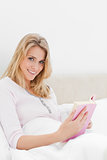 Woman in bed holding her book, looking sideways slightly and smi