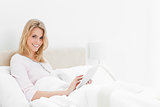 Woman sitting in bed, with tablet pc in hand, looking up and smi
