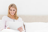 Woman sitting in bed with tablet pc, looking straight ahead and 