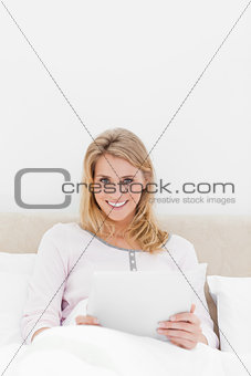 Centered shot, Woman sitting in bed with a tablet pc, looking ah