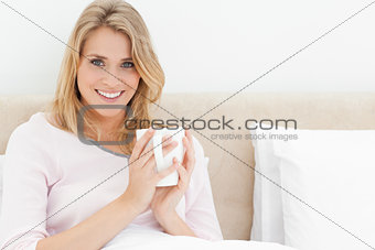 Woman sitting in bed with a cup in her hands,looking forward and
