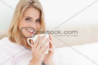 Woman holding a cup up to her lips, head turned  as she looks fo