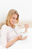 Woman in bed with a bowl of cereal, looking down at the spoon by
