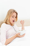 Woman in bed, with her mouth open about to eat a spoon of cereal