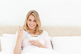 Woman in bed looking forward and smiling with a spoon and bowl o