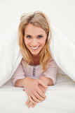 Woman in bed under a quilt, looking forward and smiling