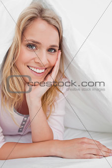 Close up, woman under the quilt smiling with her hand supporting