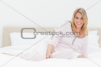 Woman lying across length of the bed, one knee folded and smilin
