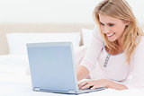 Woman lying on the bed, using a laptop and smiling