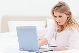 Woman lying on a bed with her laptop, looking at the screen