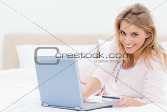 Woman lying on the bed, with a laptop in hand and looking forwar