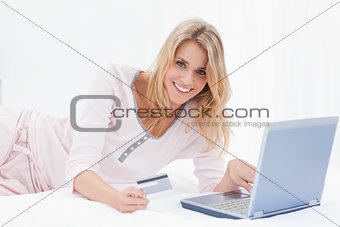 Woman lying on the bed with her laptop and credit card and smili