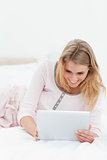 Woman lying across the bed, tablet pc in hand and smiling