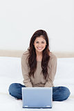 Woman sitting on the bed with the laptop in front of her and smi