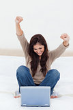 Woman celebrates with arms in the air as she looks at her laptop