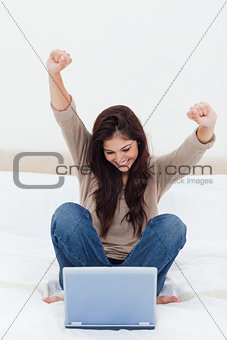 Woman celebrates with arms in the air as she looks at her laptop