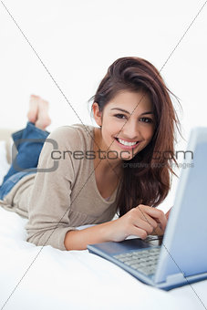 Woman smiling in front of her laptop, lying on the bed with her 