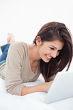 Woman smiling as she uses her tablet while lying on the bed