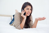 Woman making a phonecall glancing to the side as she lies on the