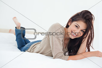 Woman lying on a bed, her hand in her hair smiling, with her leg