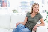 Woman sitting on couch, smiling, legs folded and looking to the 