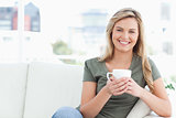 Woman smiling, holding a cup in hands and sitting on the couch