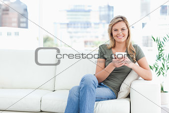 Woman sitting in the corneer of the couch, smiling with cup in h