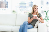 Woman sitting on the couch, with mug in hand, smiling and lookin