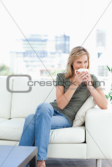 Woman with her legs crossed, holding a mug to her nose and looki