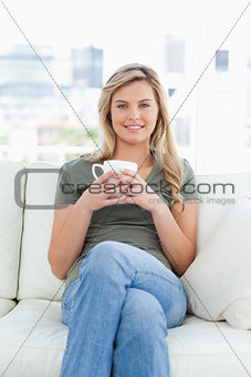 Centered shot, woman sitting on the couch with a cup in hands an