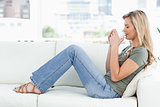 Woman sitting sideways on couch, cup raised up to her nose, eyes