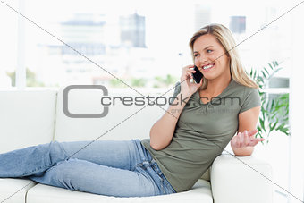 Woman smiling as she lies across the couch, making a call with a