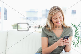 Woman sits on the couch, looking and using her phone and smiling