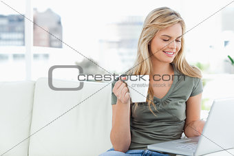 Woman smiling as she holds her cup and uses her laptop