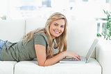 Woman smiling as she lies on the couch while using her laptop