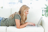 Woman lying on the couch, using her laptop and smiling