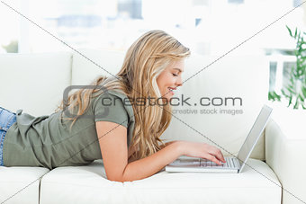 Woman lying on the couch, using her laptop and smiling