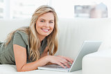 Woman lying across the couch with laptop in front of her, smilin