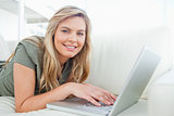 Woman looking ahead, smiling as she uses her laptop while lying 