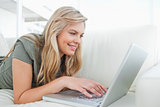 Woman smiling as she uses her laptop while lying on the couch