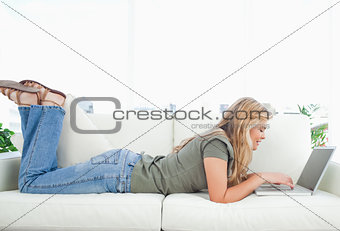 Woman lying across the couch, with legs raised and using her lap