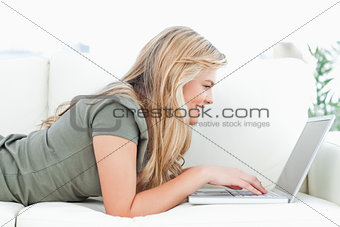 Woman using her laptop and smiling as she lies on the couch