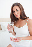 Woman looking worried as she is about to take two pills with wat