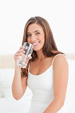 Woman smiles with a glass of water in hand raised to her mouth