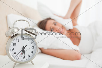 Woman covering her ears with a pillow as her alarm rings