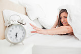 Woman under the quilt reaches out to try and silence her alarm c