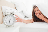 The woman yawns while trying to silence her alarm clock